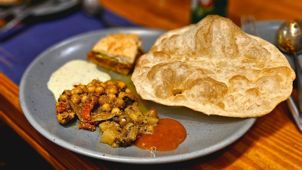services-01 A delicious Indian meal featuring puri, chole, and chutneys served on a blue plate.