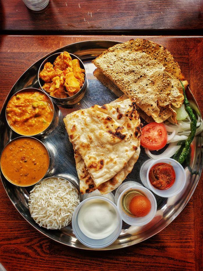 who-we-are Delicious Indian thali featuring naan, curries, and assorted dips on a tray.